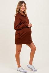 woman wearing a brown maternity zip-up sweatshirt dress and showing her baby bump