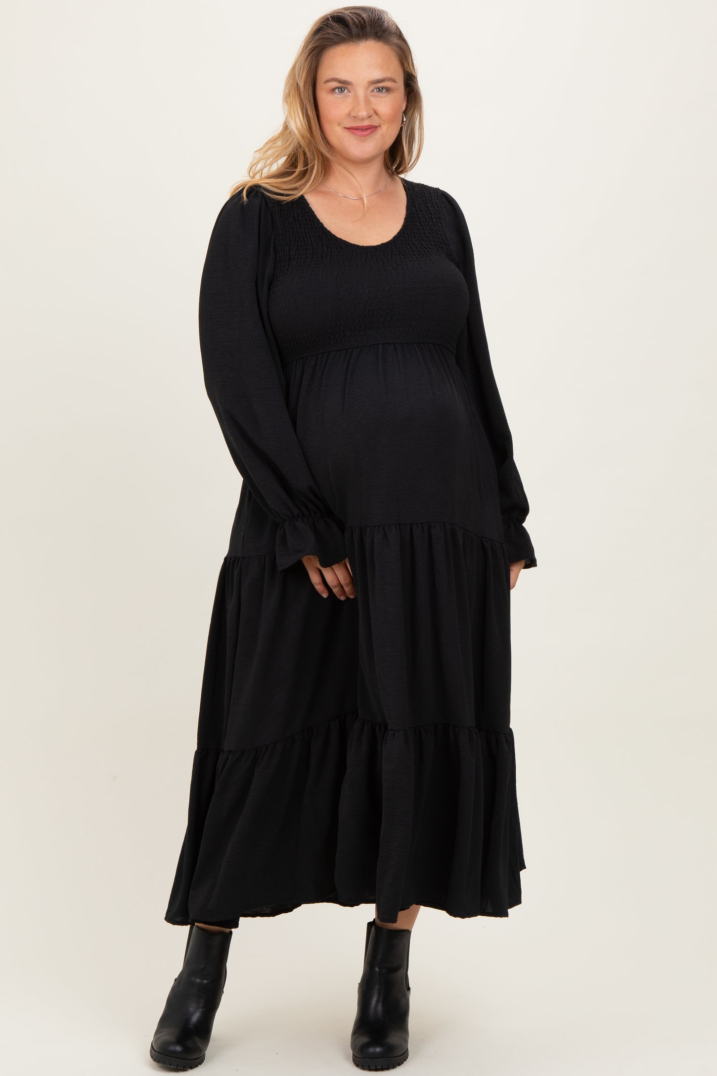 woman wearing a black long sleeve maternity dress with tiered skirt and a visible baby bump