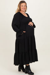 woman wearing a black tiered maternity dress with a smocked bodice and long sleeves, showing her baby bump