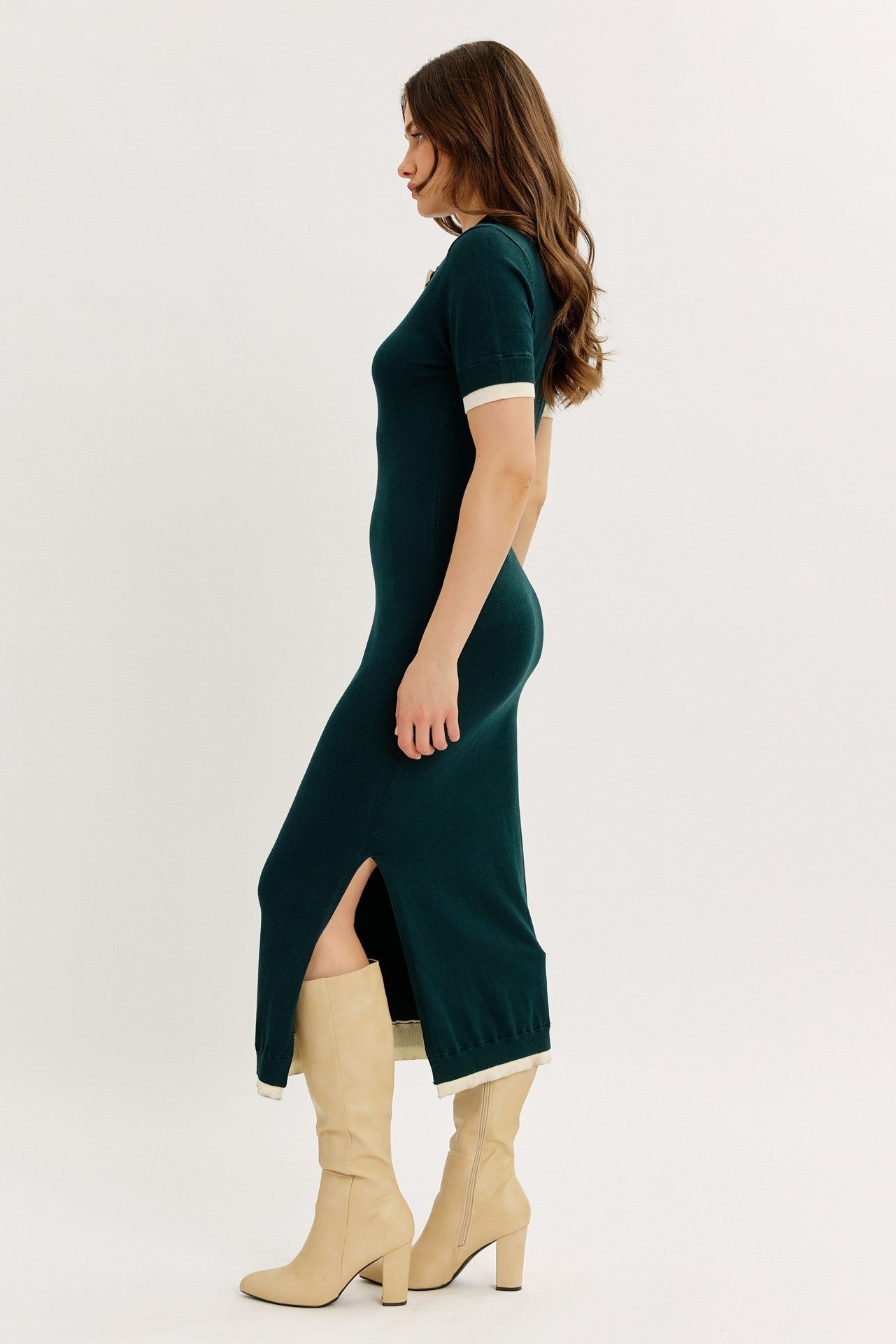 woman wearing a dark green short sleeve midi dress with side slits and beige trim, paired with knee-high beige boots