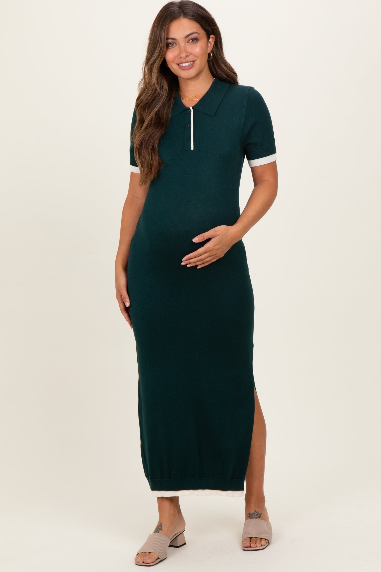 woman wearing a dark green maternity polo dress with side slits and a fitted silhouette, holding her baby bump