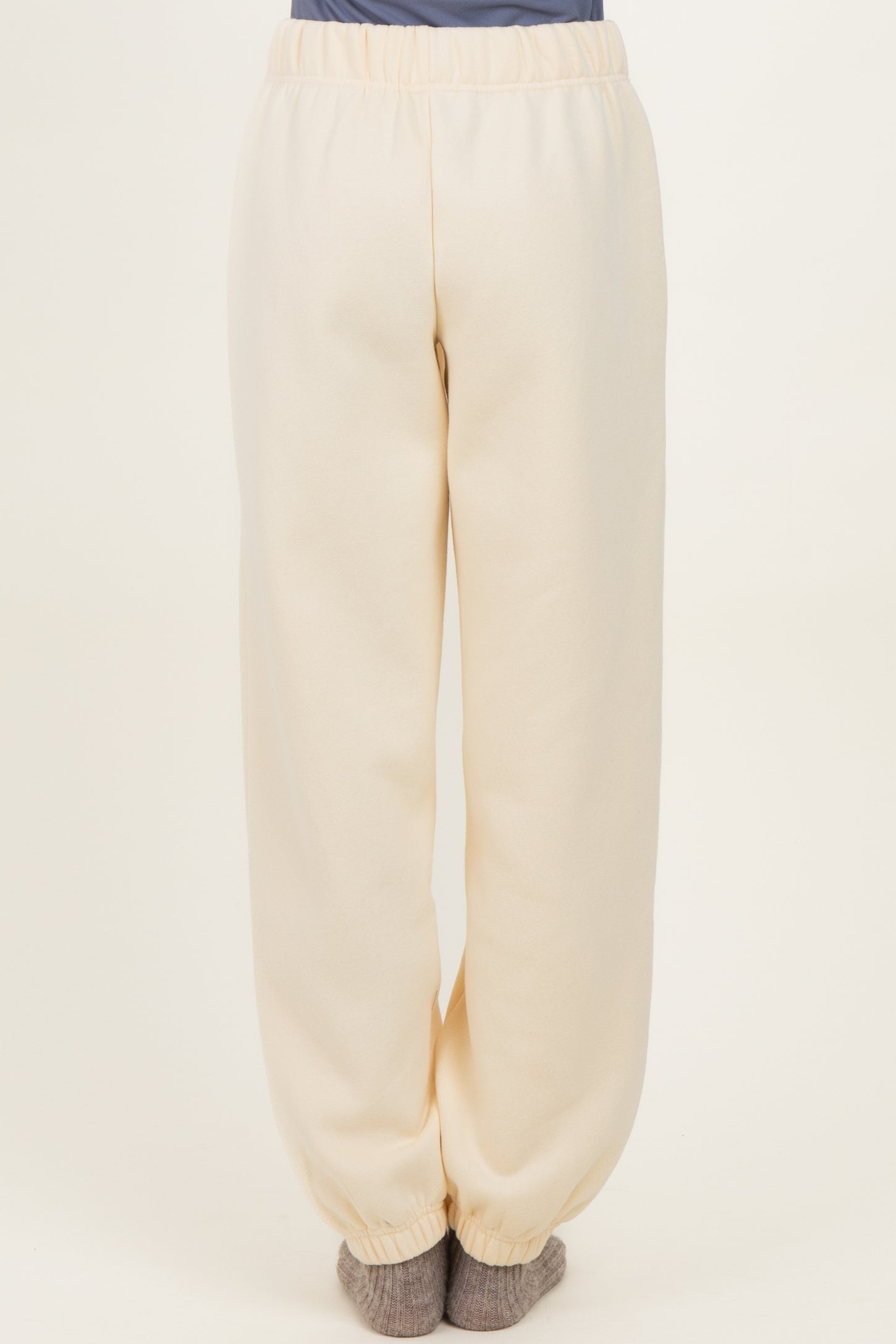 woman wearing cream-colored cozy sweatpants with elastic waistband and cuffed ankles, viewed from the back