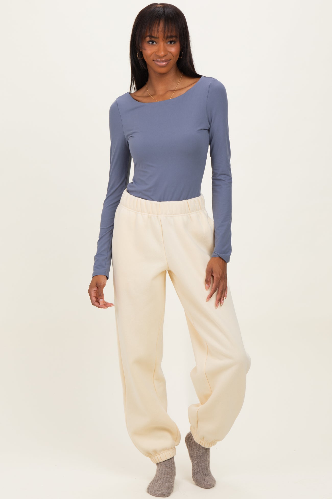 woman wearing a long sleeve blue top and cream-colored tapered sweatpants with cuffs at the ankles