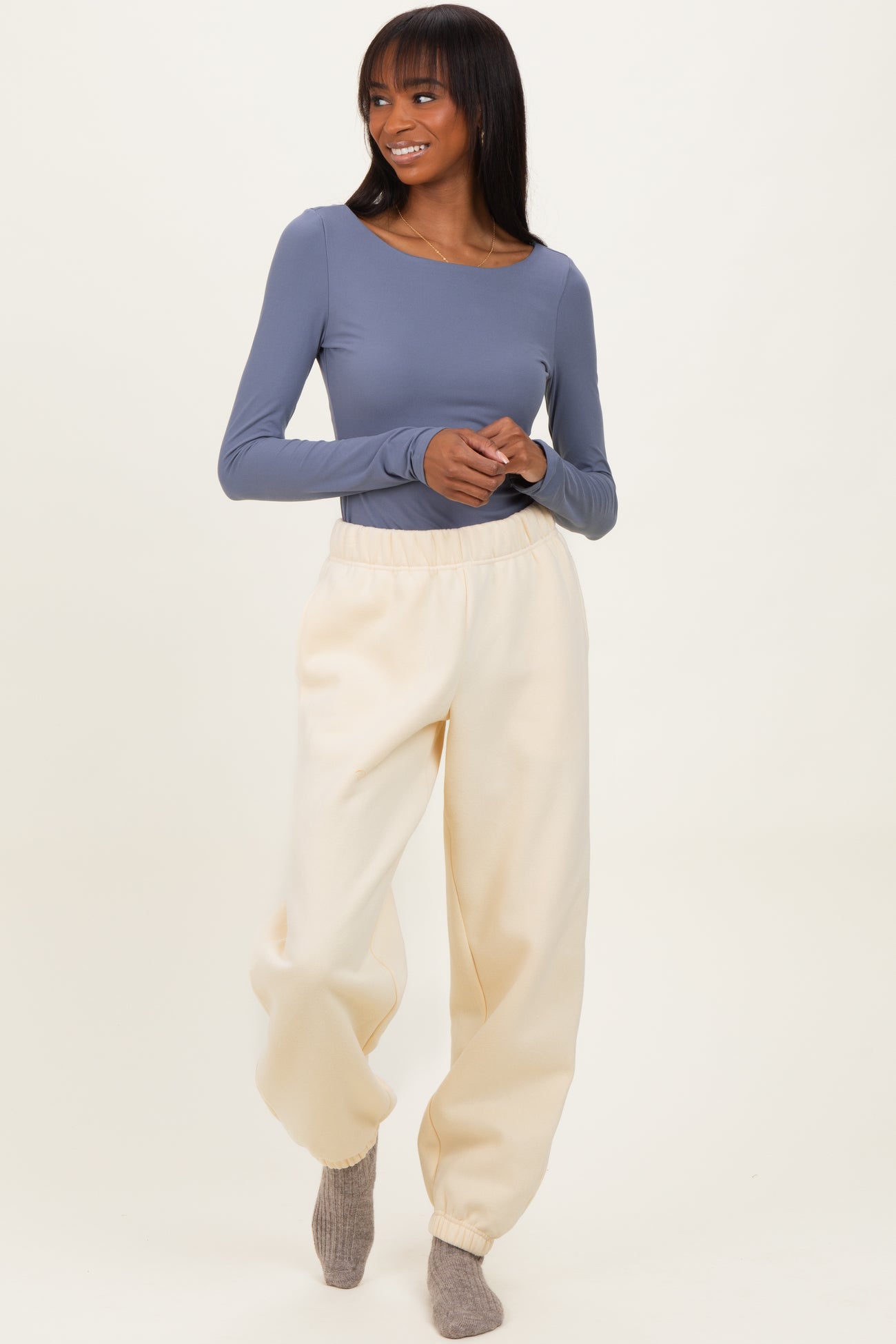 woman wearing a long sleeve gray top and cream-colored jogger pants, standing with a smile