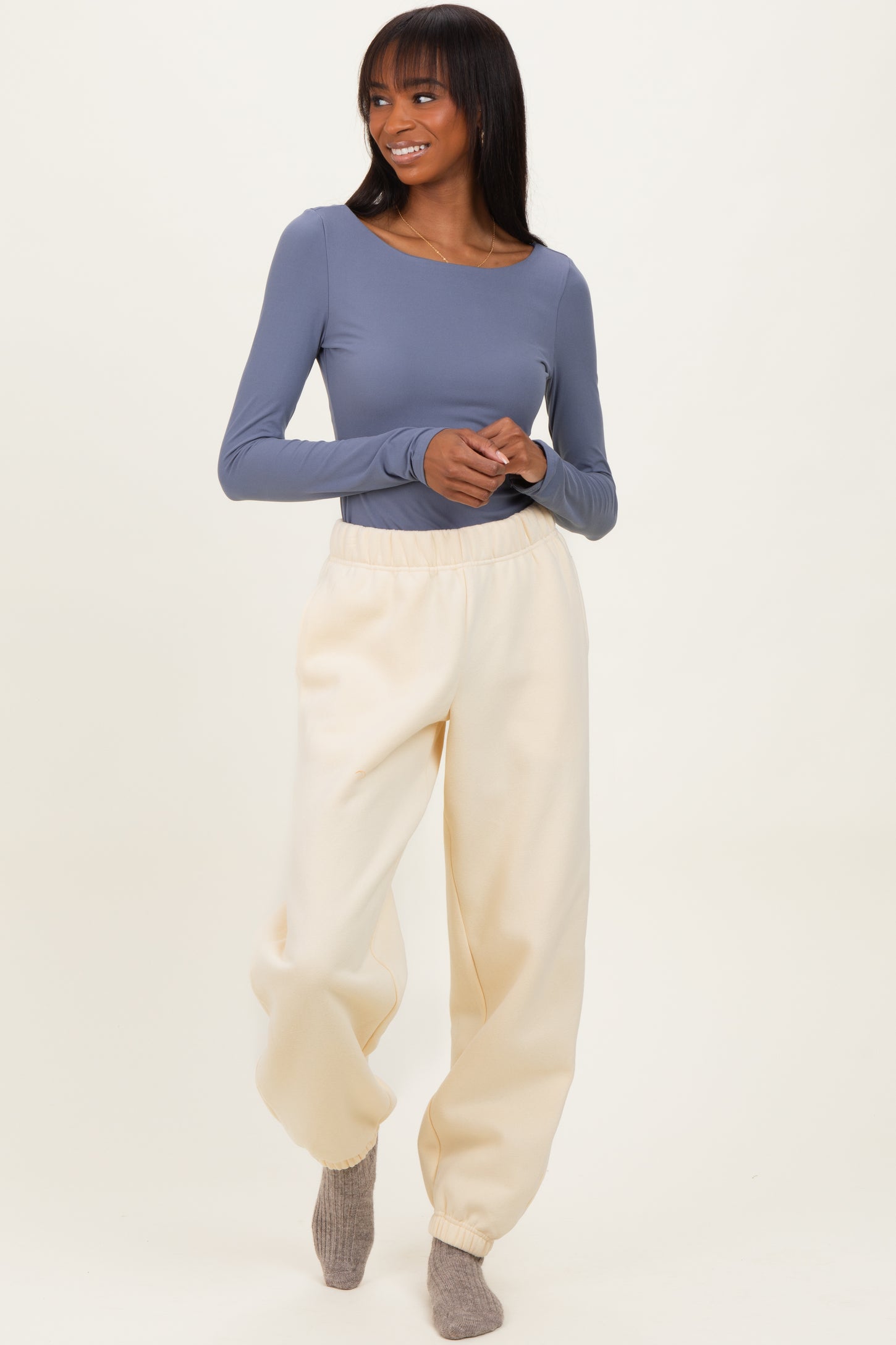 woman wearing a long sleeve gray top and cream-colored jogger pants, standing with a smile