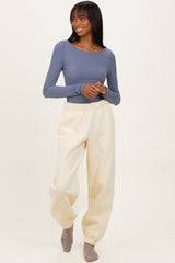 woman wearing a long sleeve gray top and cream-colored jogger pants, standing with a smile