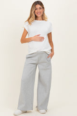 woman wearing a white ribbed maternity top and gray wide-leg sweatpants, holding her baby bump