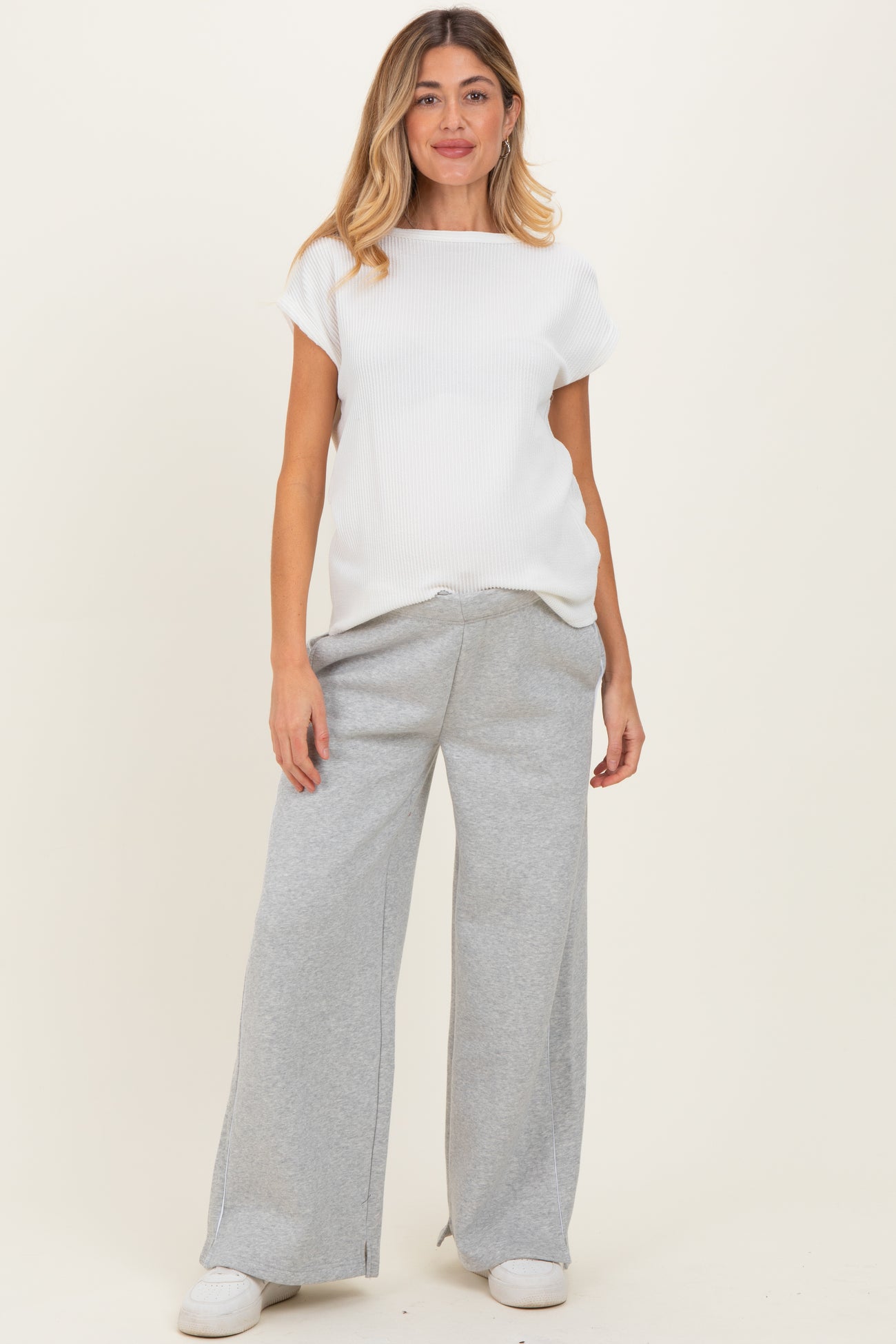 woman wearing a white ribbed maternity top and gray wide-leg sweatpants, showing her baby bump