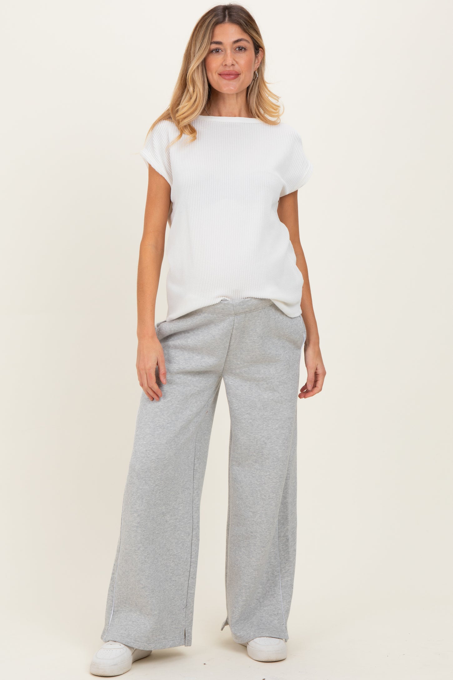 woman wearing a white ribbed maternity top and gray wide-leg sweatpants, showing her baby bump