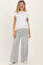 woman wearing a white ribbed maternity top and gray wide-leg sweatpants, showing her baby bump