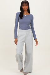 woman wearing a gray long sleeve top and light gray wide-leg sweatpants, smiling while walking toward the camera