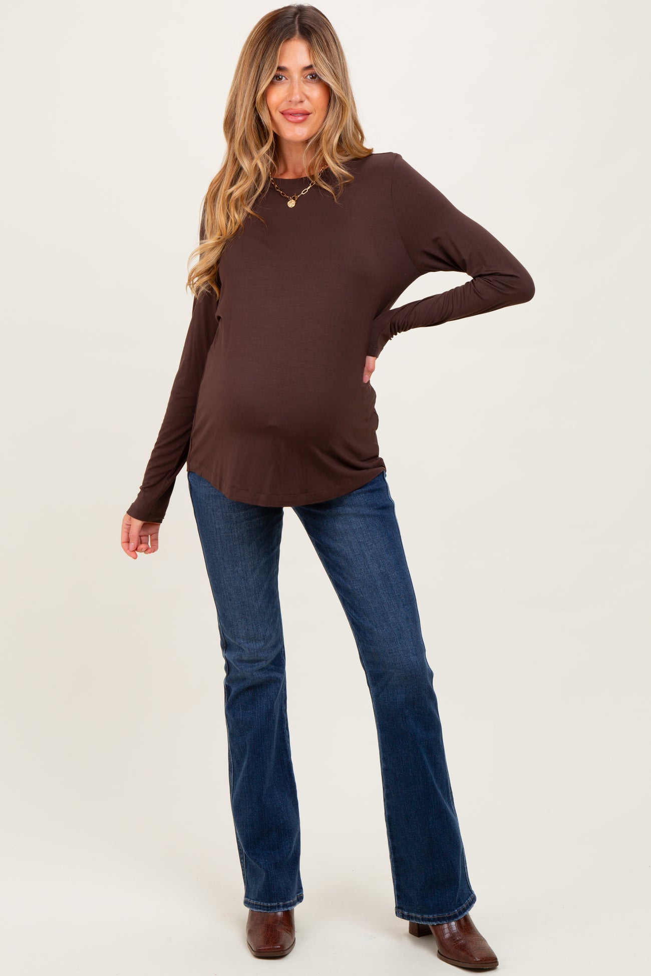 woman wearing a brown long sleeve maternity top and blue flared jeans with a visible baby bump