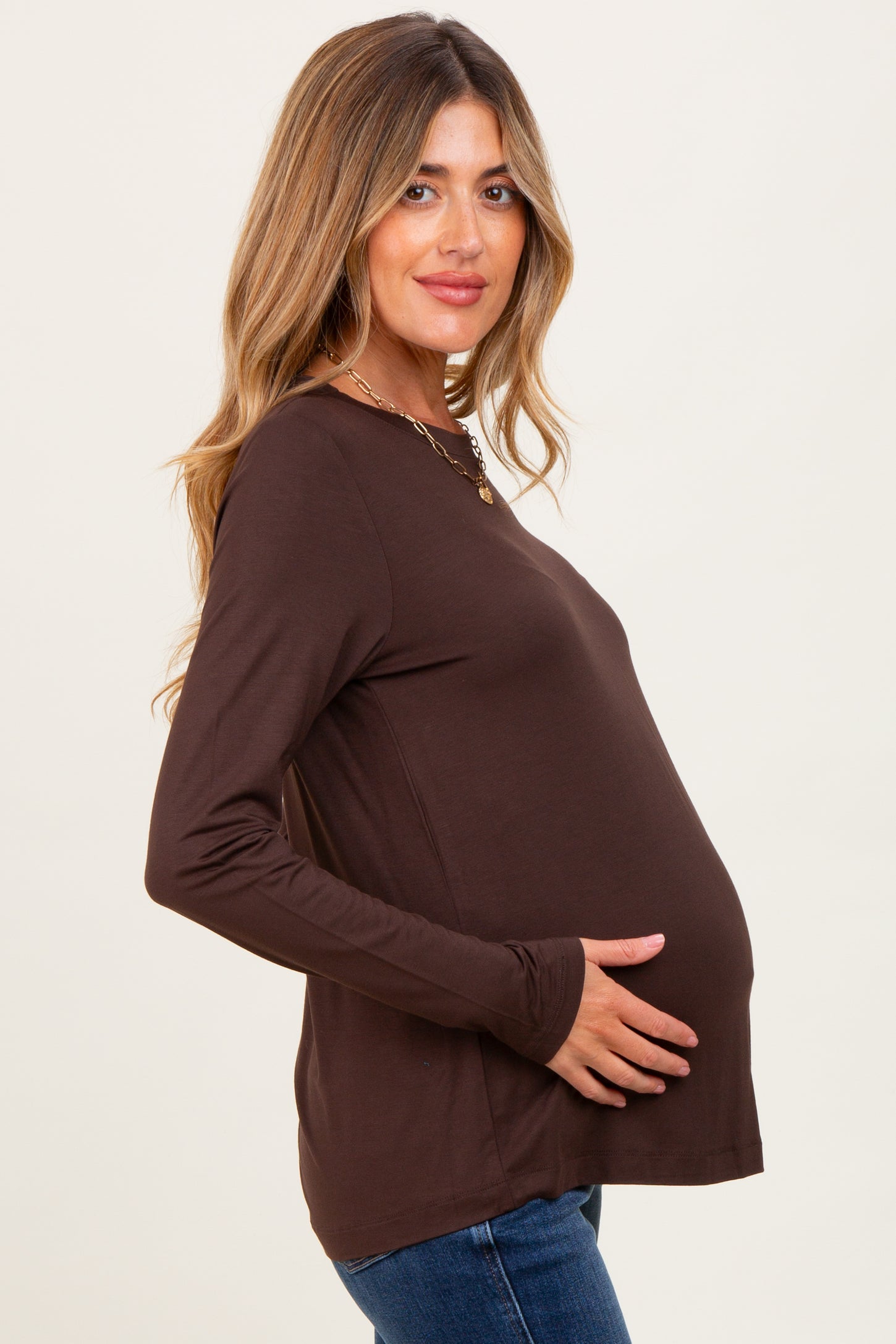 woman wearing a brown long sleeve maternity top and holding her baby bump