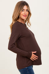 woman wearing a brown long sleeve maternity top and holding her baby bump