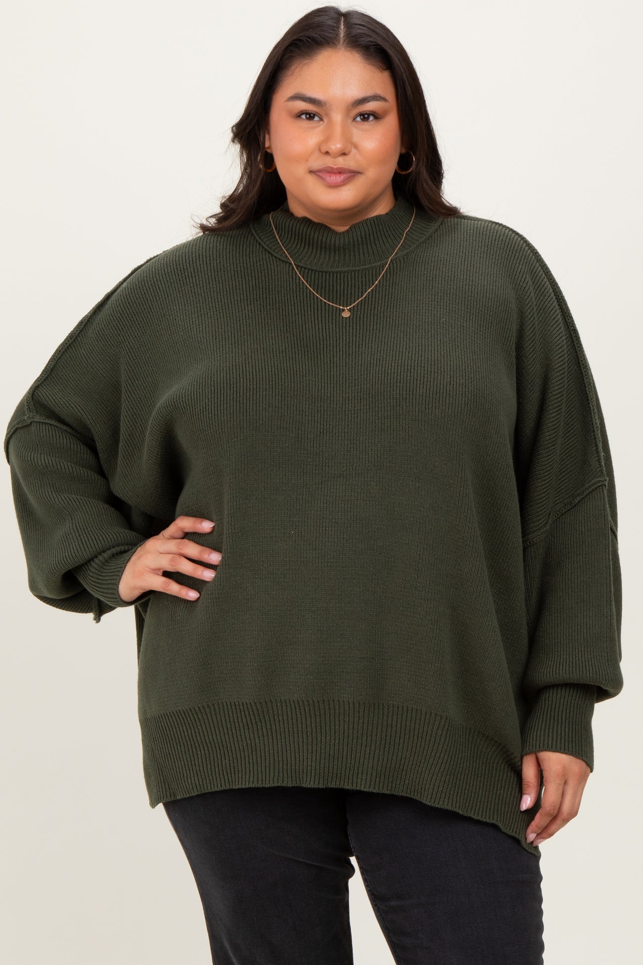 woman wearing an oversized olive green ribbed sweater with a high neckline and relaxed fit, posing confidently
