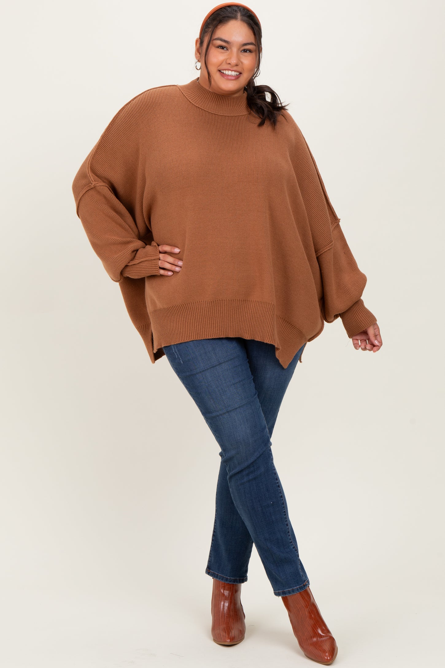 woman wearing a oversized brown sweater with a high neck and relaxed fit, paired with skinny blue jeans and heeled boots