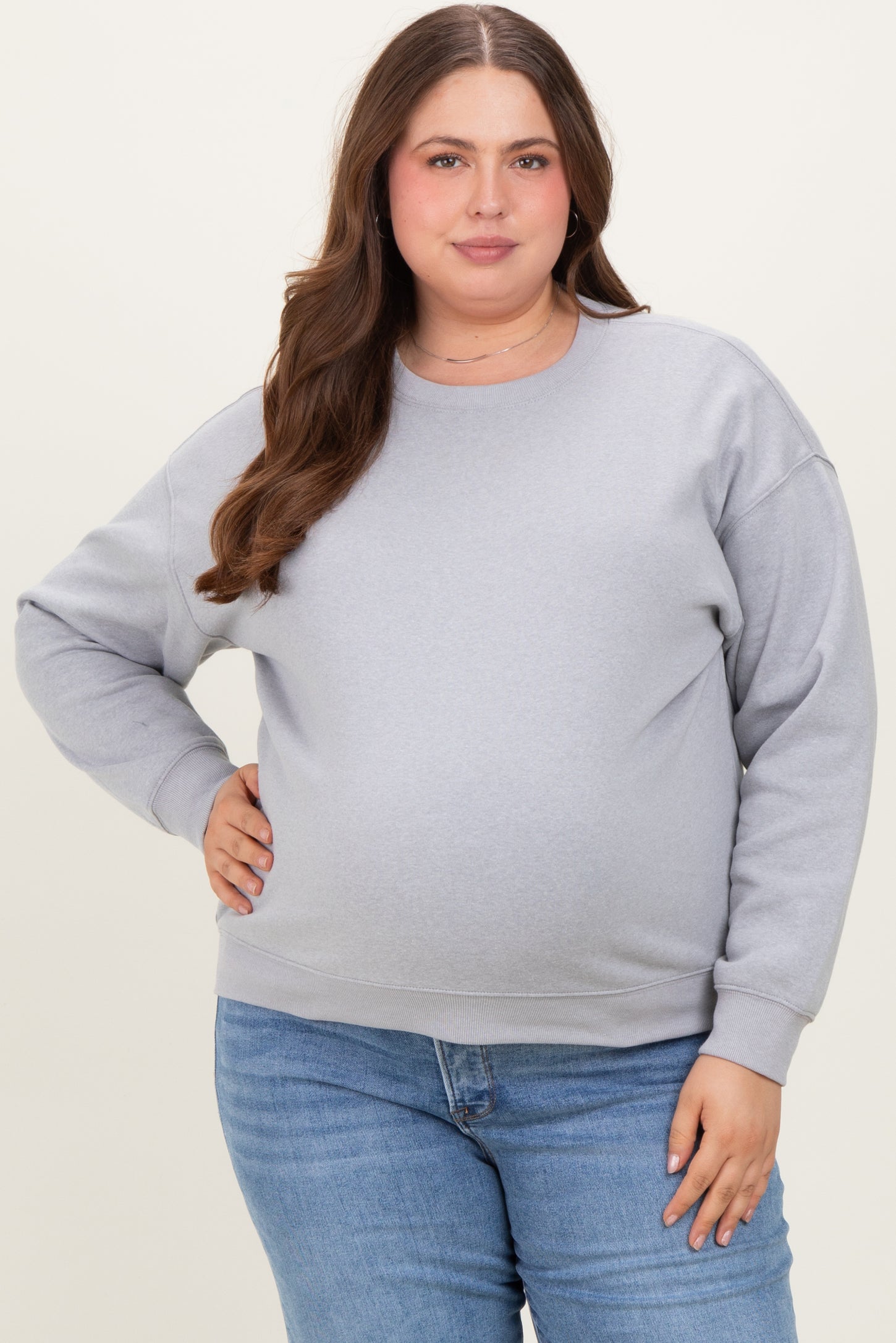 woman wearing a light gray maternity sweatshirt and blue jeans, showcasing her baby bump