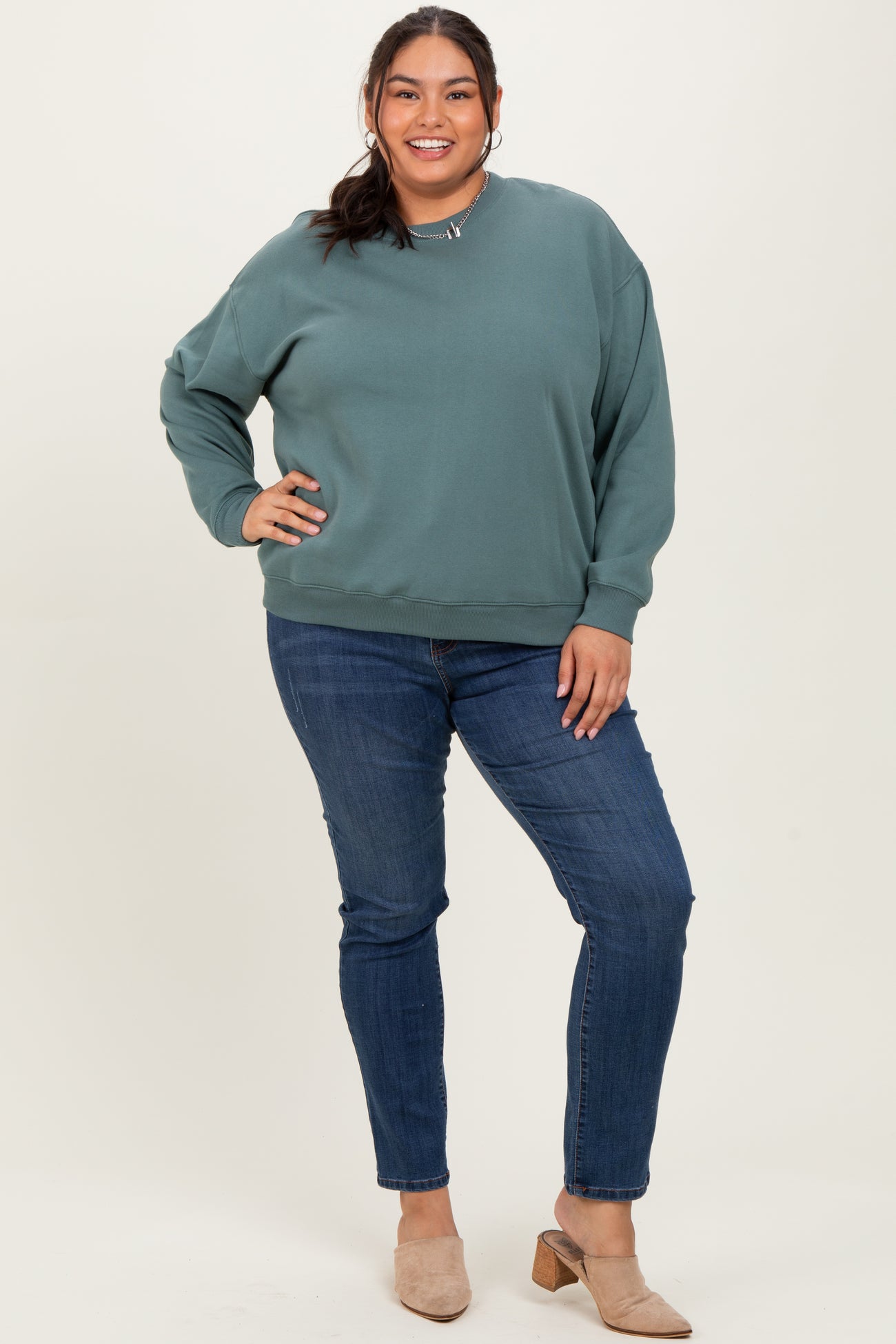 woman wearing a teal oversized sweatshirt with a relaxed fit and blue skinny jeans, standing and smiling