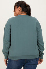 woman wearing a teal oversized sweatshirt with dropped shoulders, viewed from the back, paired with blue jeans