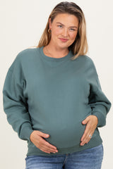 woman wearing a green maternity plus sweatshirt and holding her baby bump