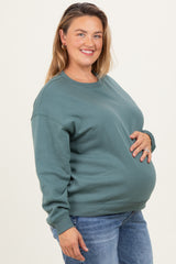 woman wearing a green maternity sweatshirt and holding her baby bump, paired with jeans