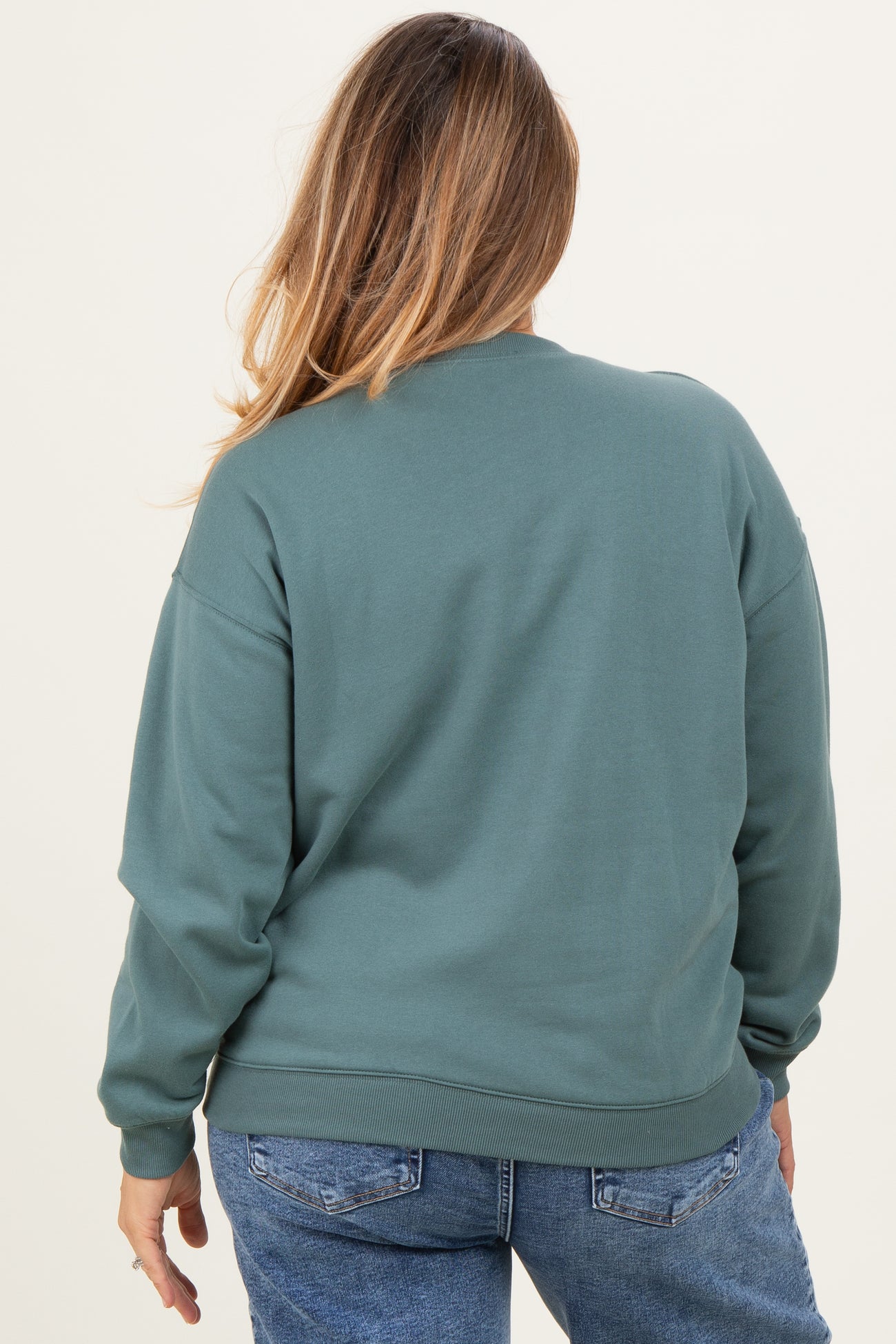 woman wearing a green maternity plus crewneck sweatshirt, viewed from the back, with loose fit and ribbed hem