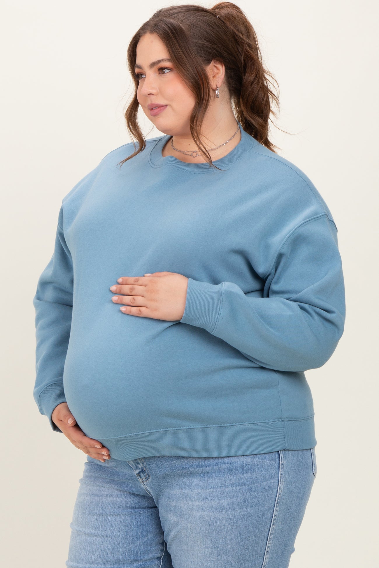woman wearing a blue maternity plus sweatshirt with a visible baby bump, paired with light blue jeans
