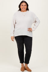 woman wearing a light beige oversized sweater and black slim-fit jeans, posing with brown slip-on shoes