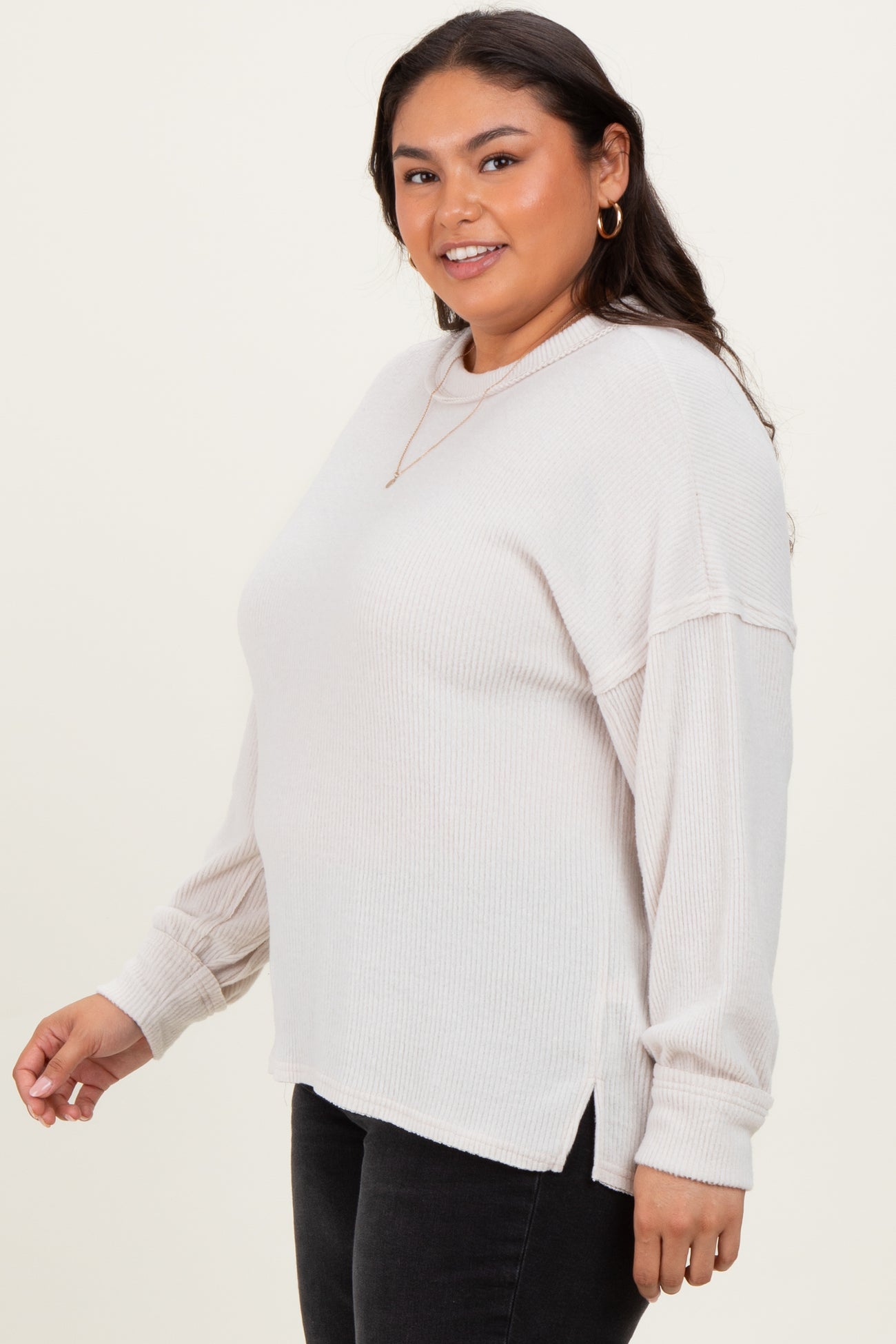 woman wearing a light beige oversized ribbed sweater with side slits and long sleeves