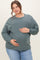 woman wearing a green oversized maternity sweatshirt and gently holding her baby bump