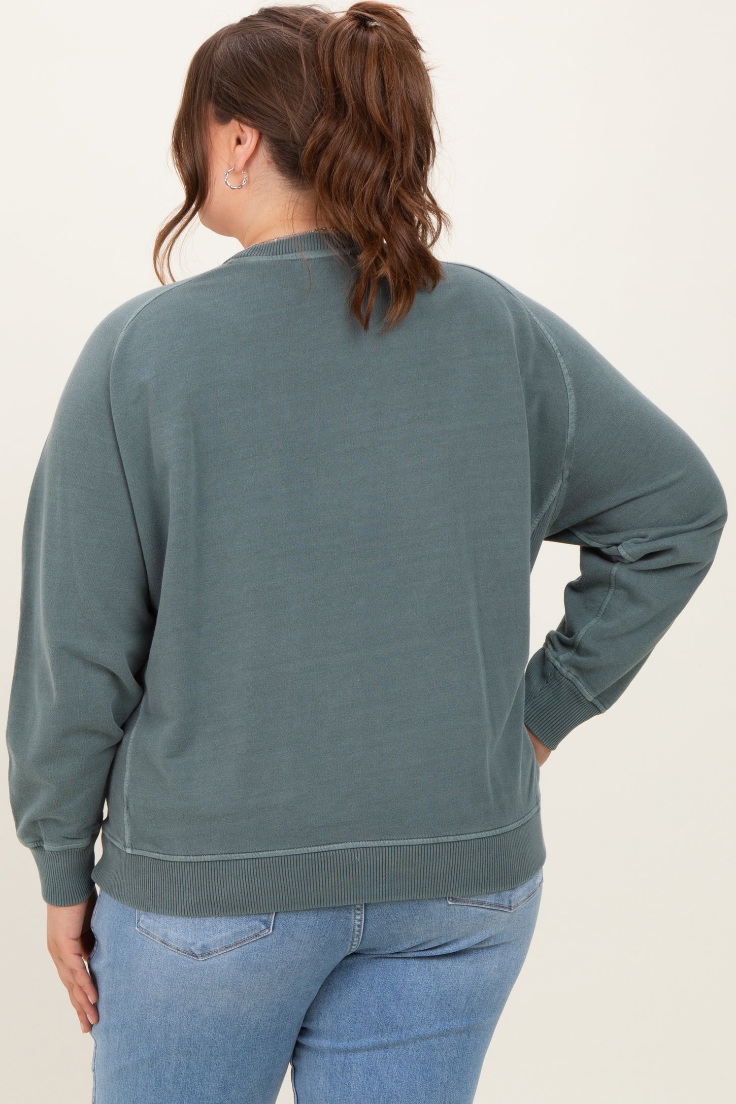 woman wearing a green oversized maternity plus sweatshirt, seen from the back, styled with light blue jeans