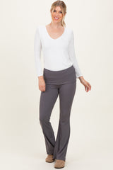 woman wearing a white long sleeve v-neck top and gray flared pants, smiling and standing against a light background