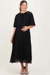 woman wearing a black pleated maternity dress with a cape detail and holding her baby bump