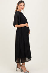 woman wearing a black pleated maternity dress with flutter sleeves and holding her baby bump