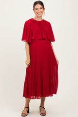 woman wearing a red pleated maternity dress with a cape detail and a visible baby bump