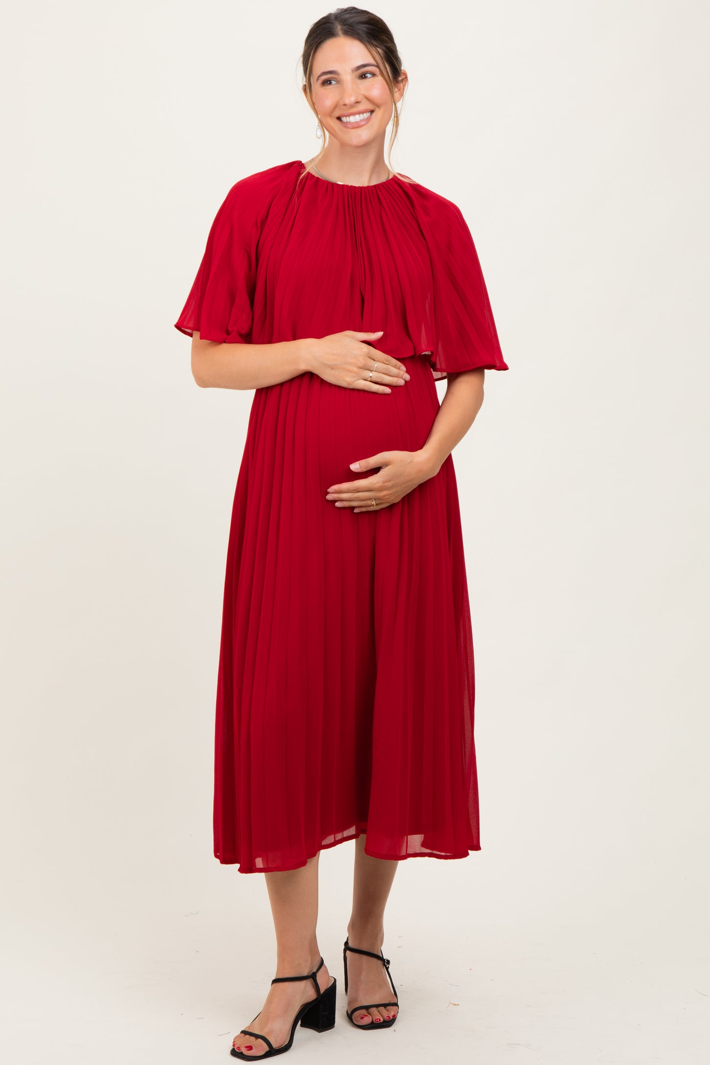 woman wearing a red pleated maternity dress and holding her baby bump