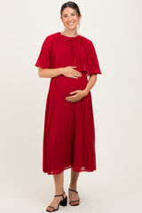 woman wearing a red pleated maternity dress and holding her baby bump