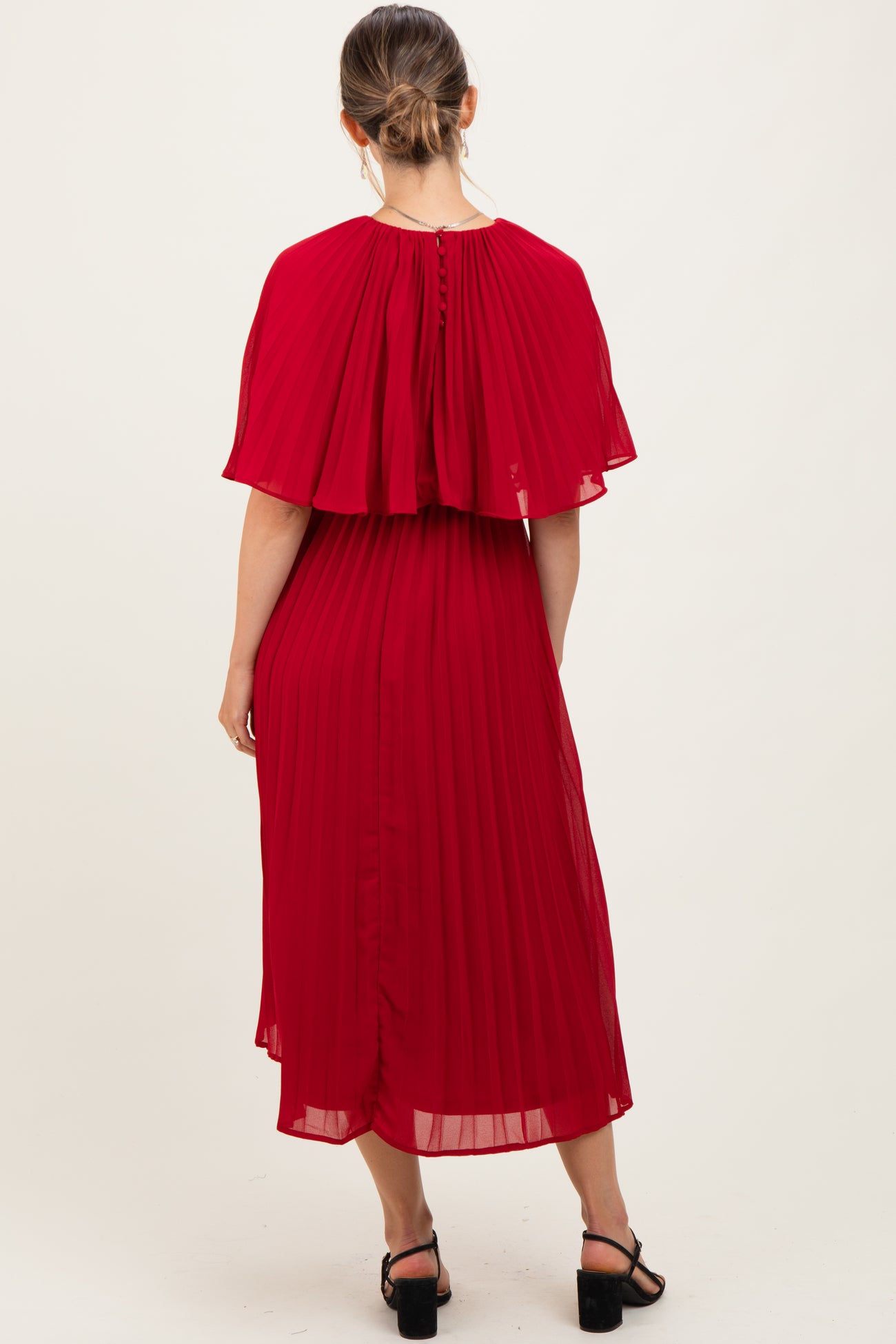 woman wearing a red pleated maternity dress with a cape-style overlay and buttons at the back