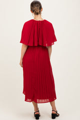 woman wearing a red pleated maternity dress with a cape-style overlay and buttons at the back