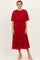 woman wearing a red pleated midi dress with a cape-style top and nude heeled sandals