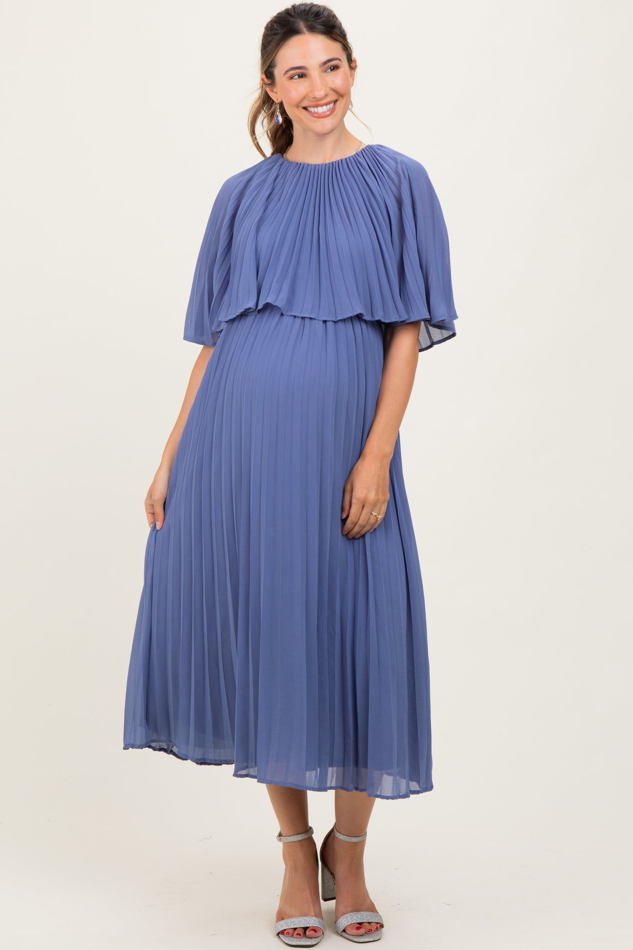 woman wearing a lavender pleated maternity dress with a cape-style top and a visible baby bump