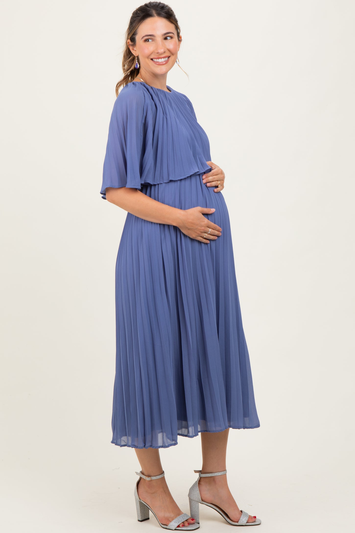 woman wearing a pleated lavender maternity dress, showcasing her baby bump, standing in a relaxed pose