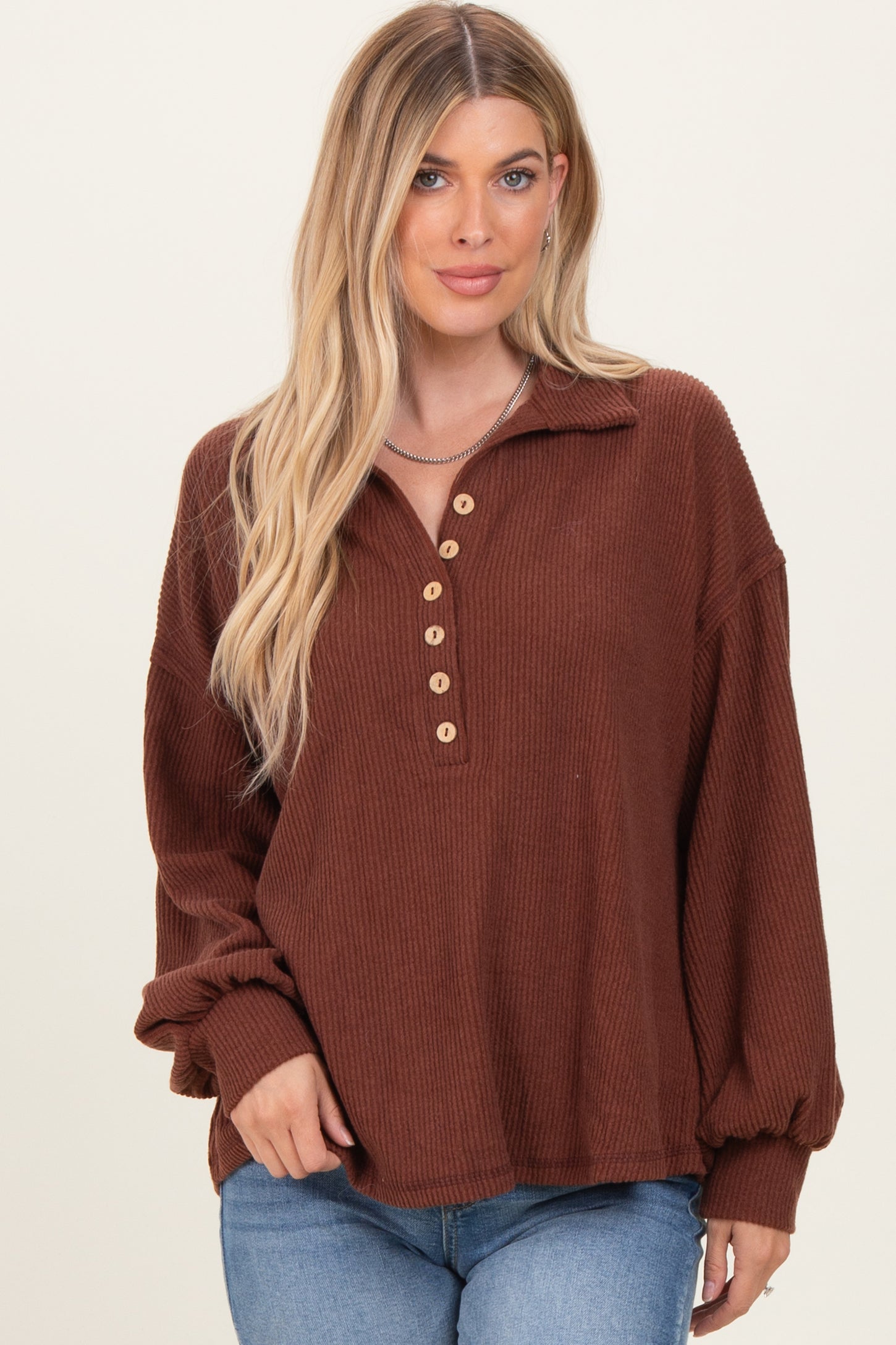 woman wearing a brown ribbed long sleeve top with a collar and button detail, paired with blue jeans