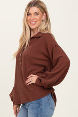 woman wearing a brown ribbed long sleeve top with a collar and button details, paired with blue jeans