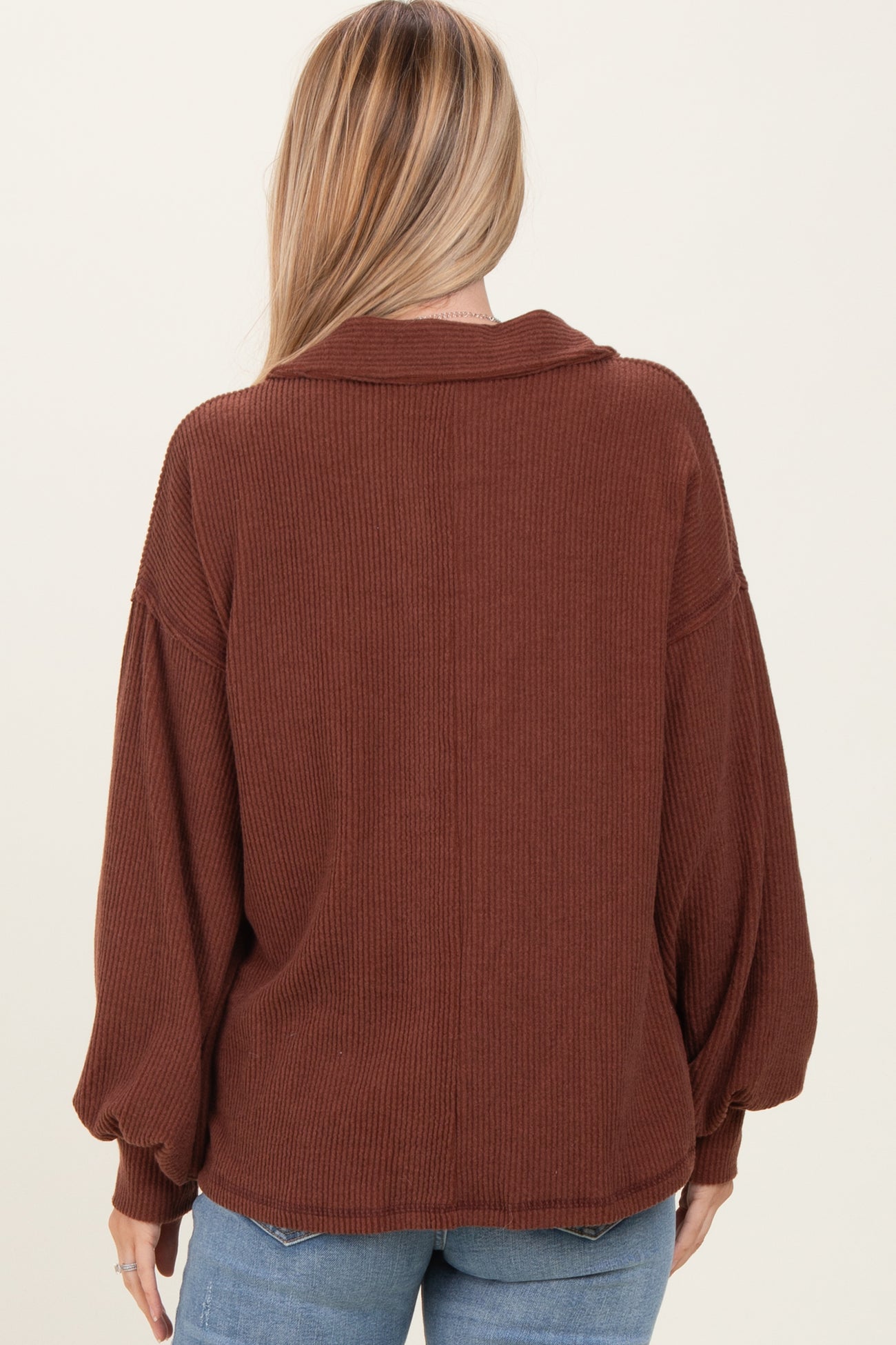 woman wearing a rust-colored oversized ribbed sweater with a collar and balloon sleeves, viewed from the back
