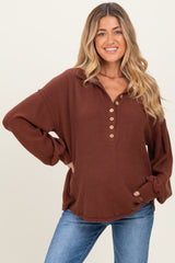 woman wearing a rust brown maternity top with a henley neckline and button details, styled with blue jeans