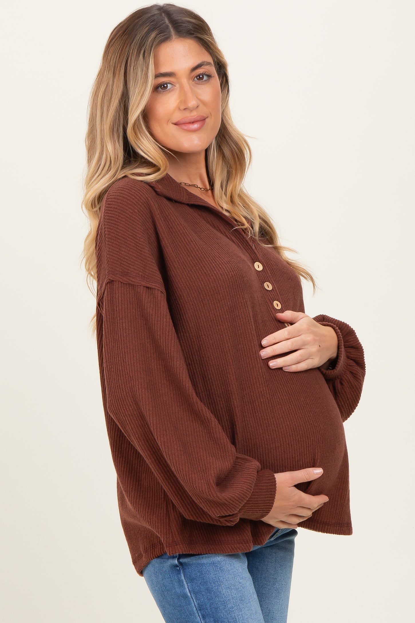 woman wearing a brown ribbed long sleeve maternity top with buttons and holding her baby bump