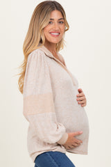 woman wearing a beige maternity sweater with a half zip and balloon sleeves, holding her baby bump