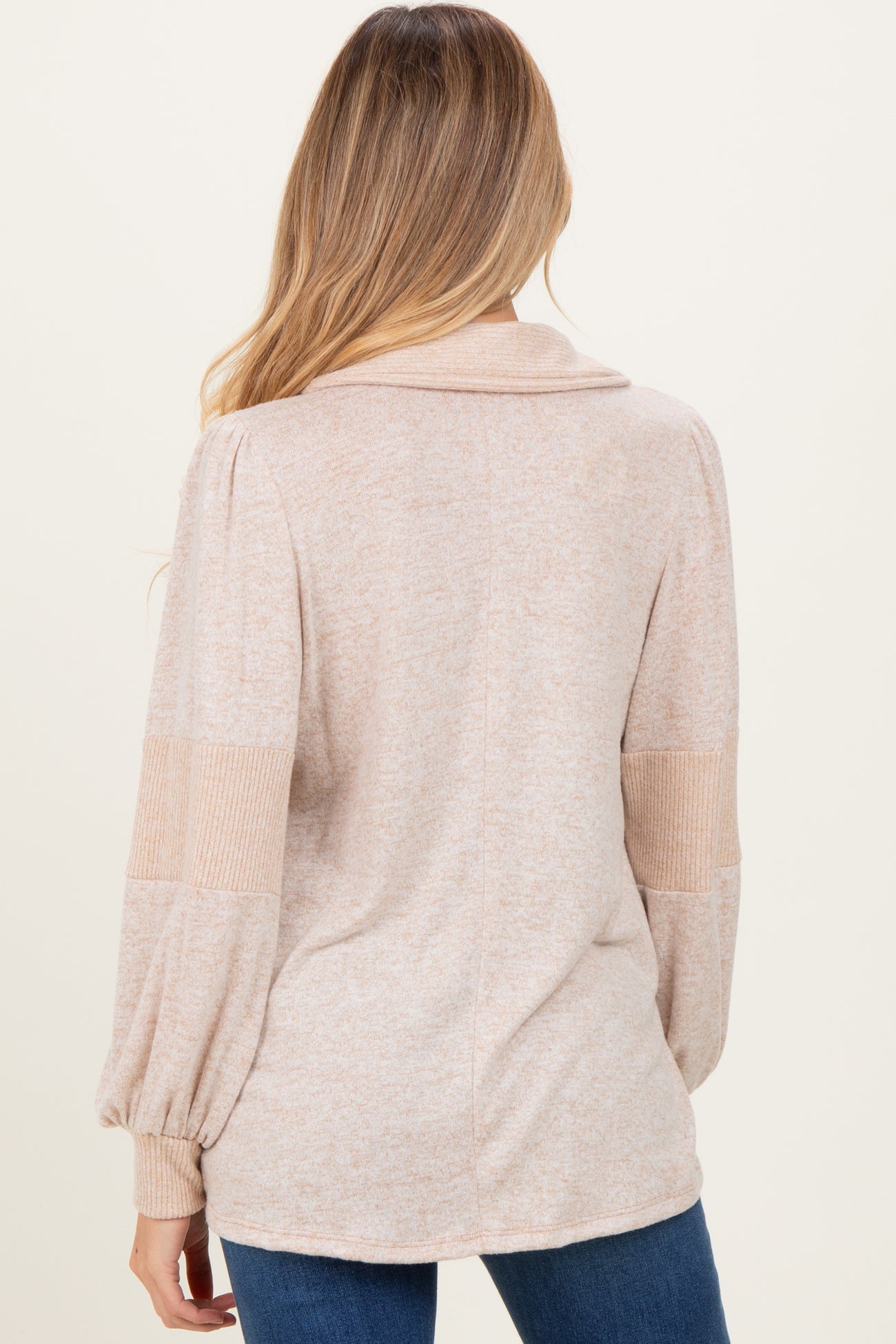 woman wearing a beige maternity sweater with a shawl collar and balloon sleeves, showing a relaxed fit from the back