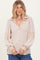 woman wearing a beige long sleeve pullover top with a v-neck and ribbed sleeves, styled casually with jeans
